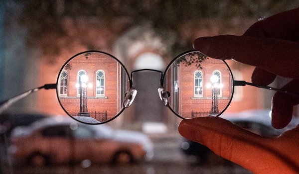 Person with poor vision comparing their view of the building across the street with and without their corrective glasses.